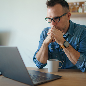 Fiatal férfi elgondolkodva figyeli a laptopja kijelzőjét