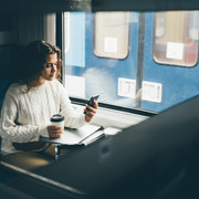 woman on train drinking coffee using mobile phone